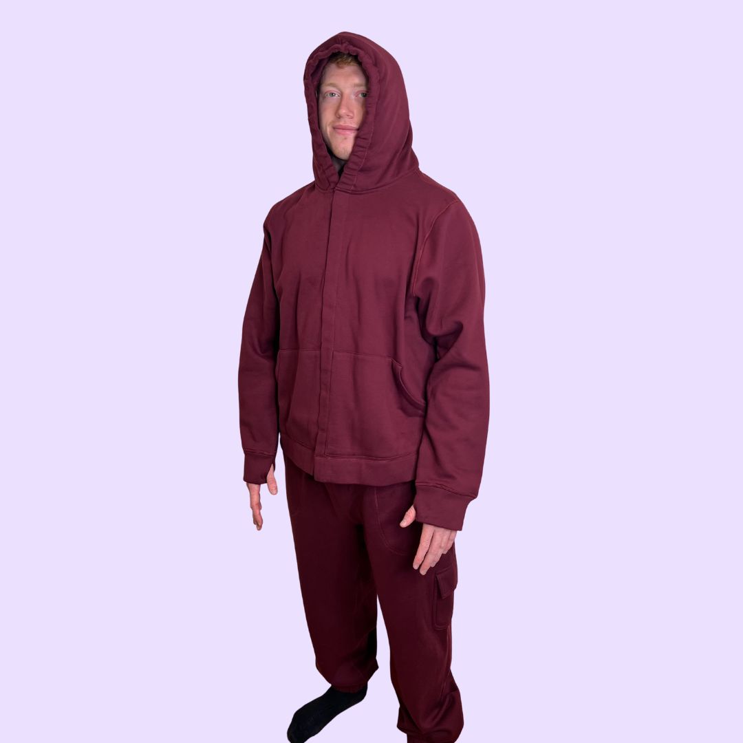 Man wearing a maroon sound reducing hoodie and pants on a light purple background