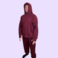 Man wearing a maroon sound reducing hoodie and pants on a light purple background