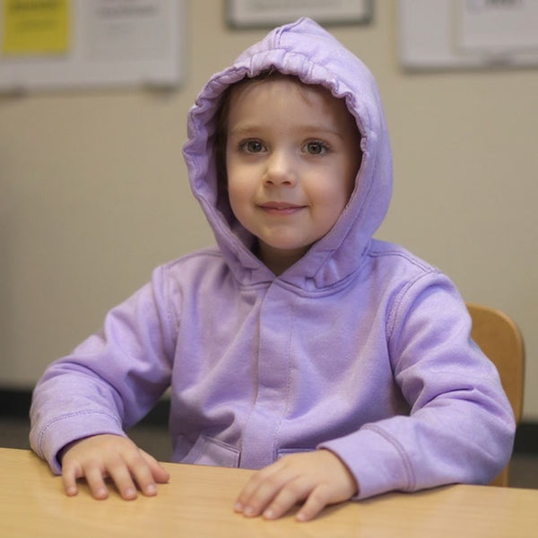 A child sitting in a classroom wearing the QuietSense sensory hoodie with the magnetic closures fastened and the sound-reducing hood pulled up over their head