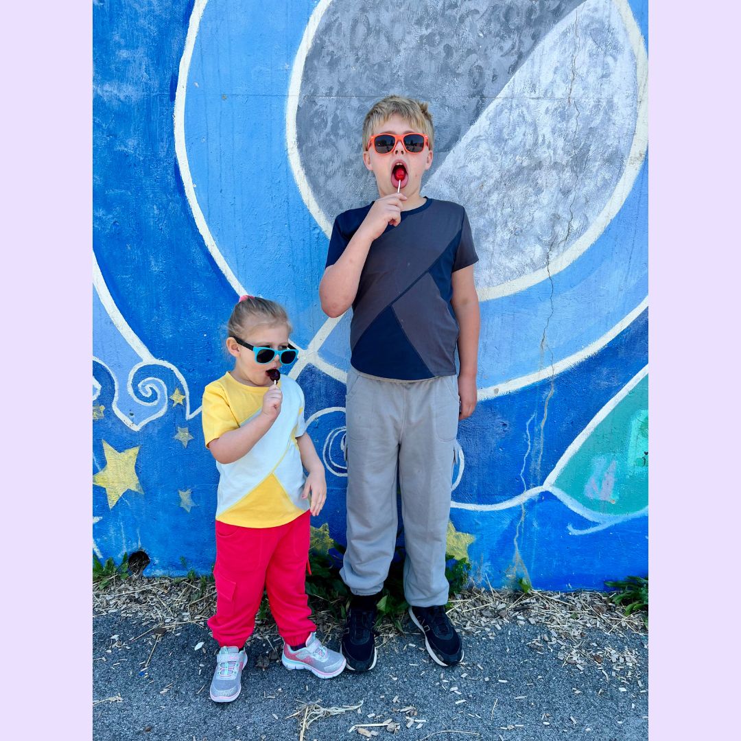 Two children posing in front of a colorful mural with sunglasses on in sensory friendly clothing.