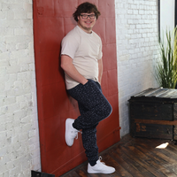 Adult with down syndrome in sensory friendly fidget joggers with hands in pocket leaning against the wall.