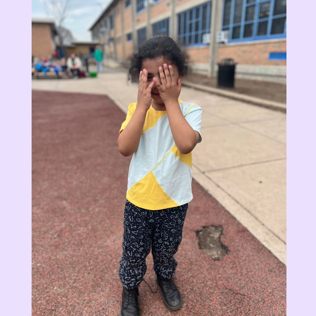 Child covering face with hands on a school playground wearing colorful sensory clothing