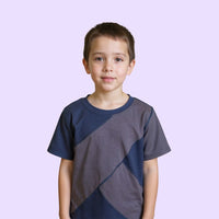 Child wearing a gray and navy blue sensory friendly shirt on a light purple background