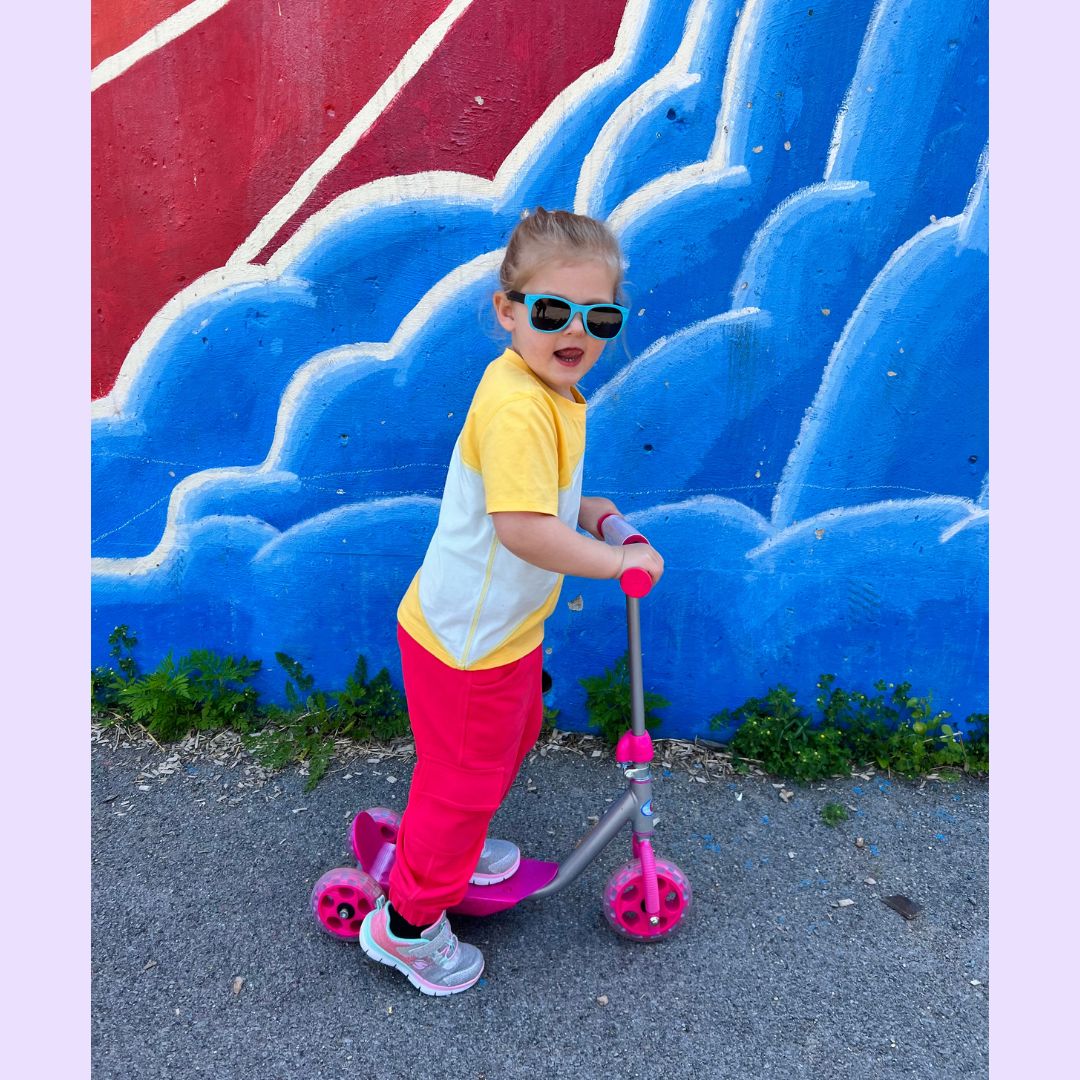 Child on a scooter in front of a colorful wall with blue and red design