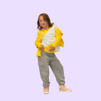 Child with down syndrome wearing a yellow and gray outfit on a light purple background
