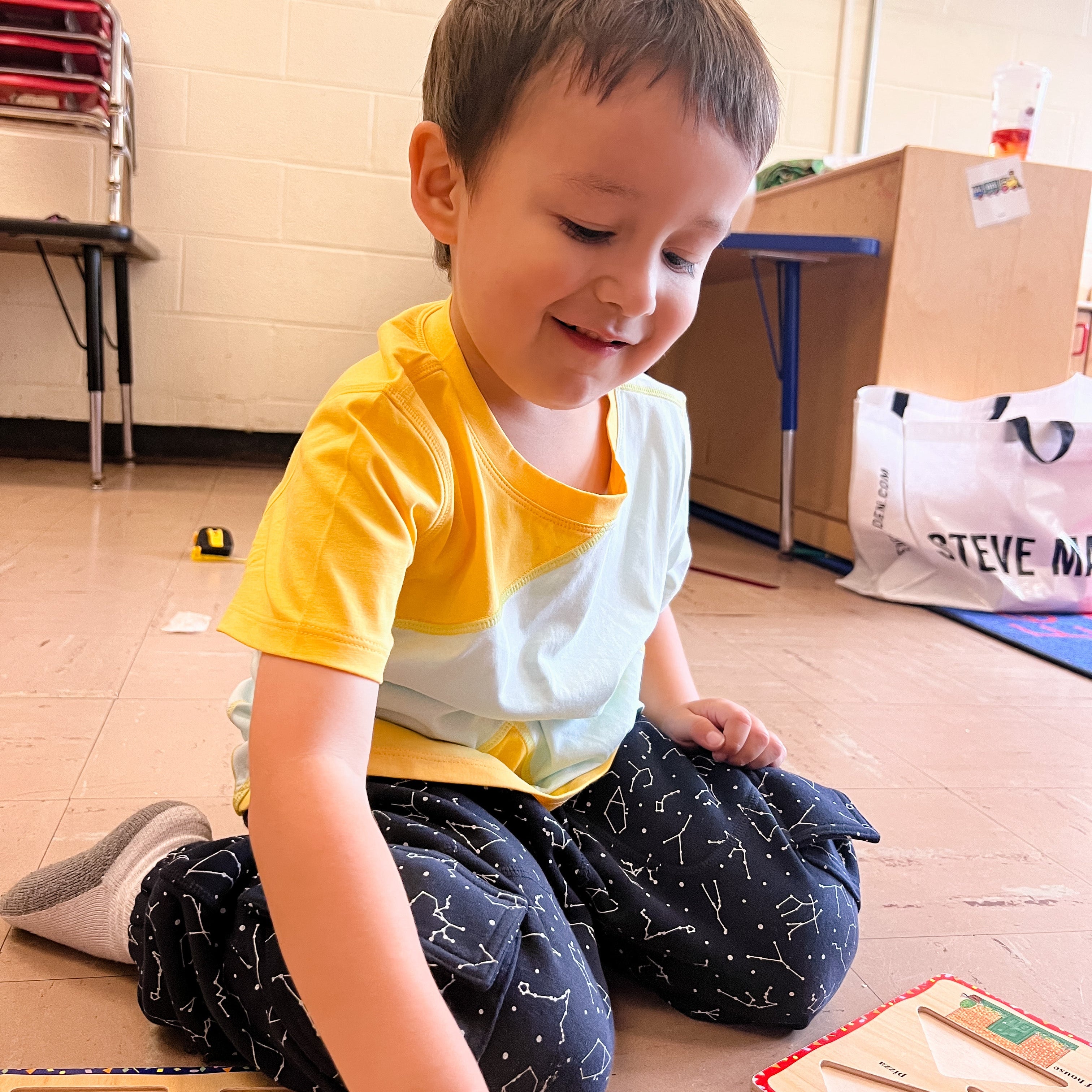 Autistic child sitting on the floor with educational materials in a classroom setting wearing sensory friendly clothing