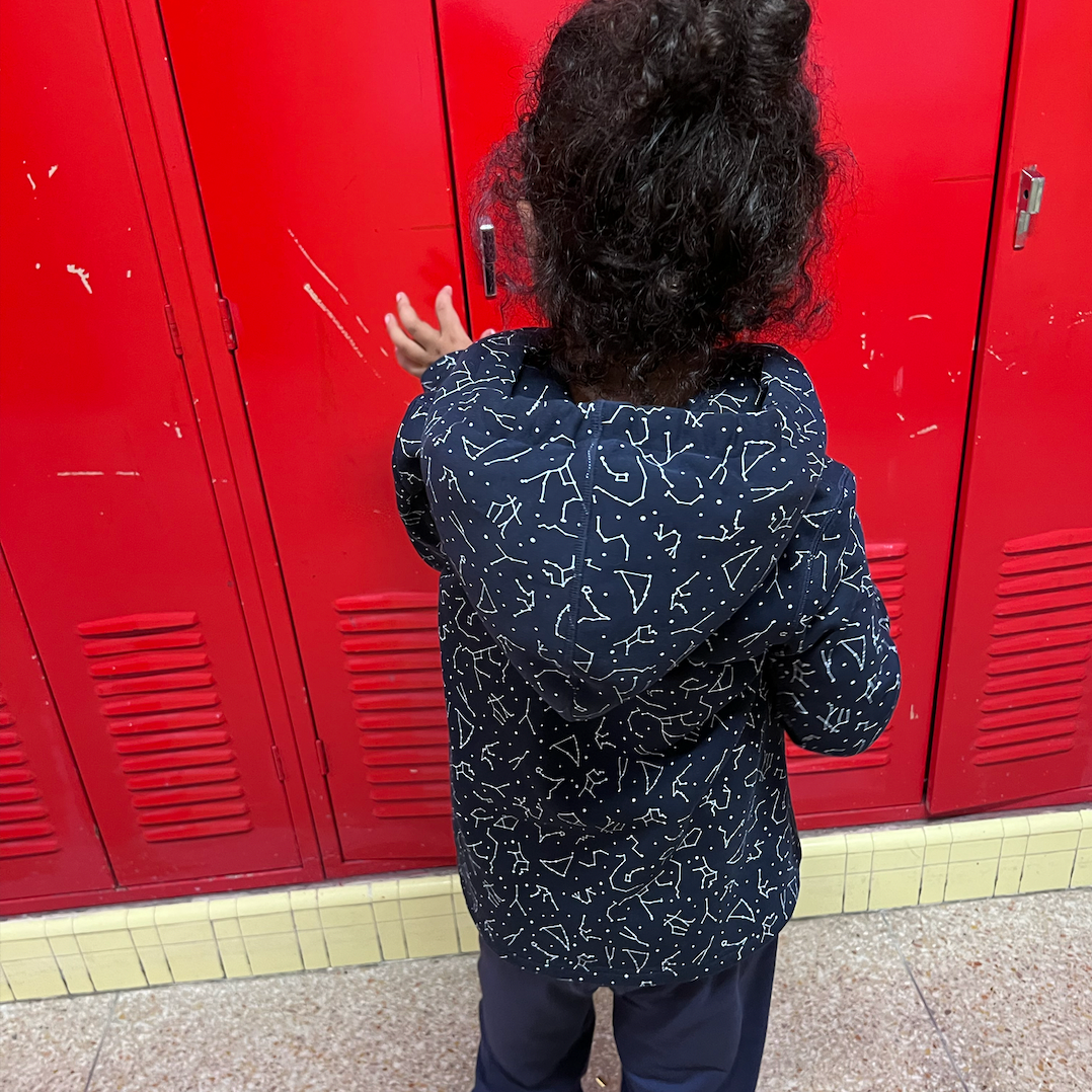 Autistic child at school in constellation print sound reducing sensory jacket in front of red lockers.