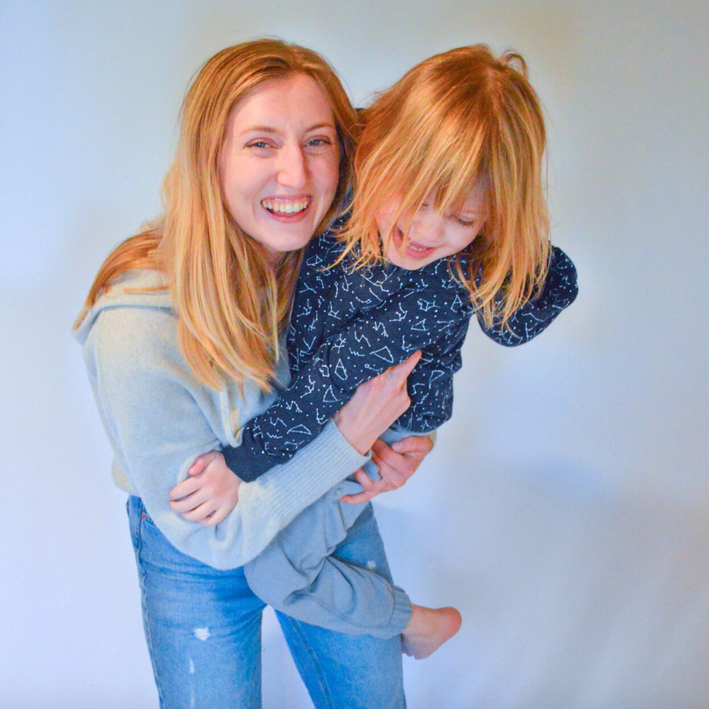 Julia in jeans and a sweater holding autistic model, girl age 5, in our sensory clothing.